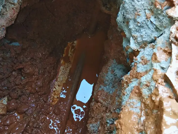 Abertura no piso com água acumulada sobre o cano danificado